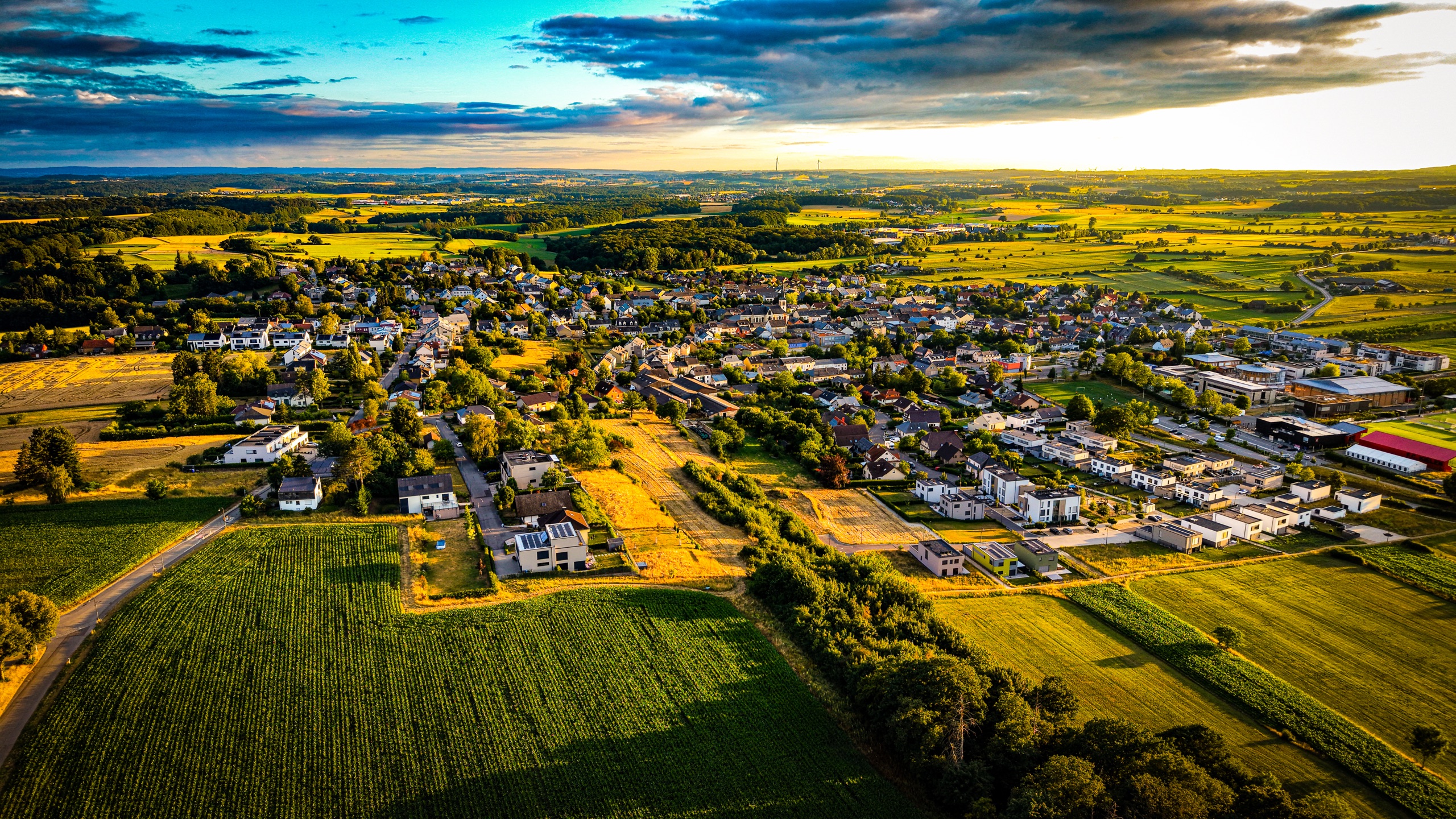 The village of Marienthal from altitude at golden hour — church spire, slate rooftops, and surrounding harvest fields glowing amber