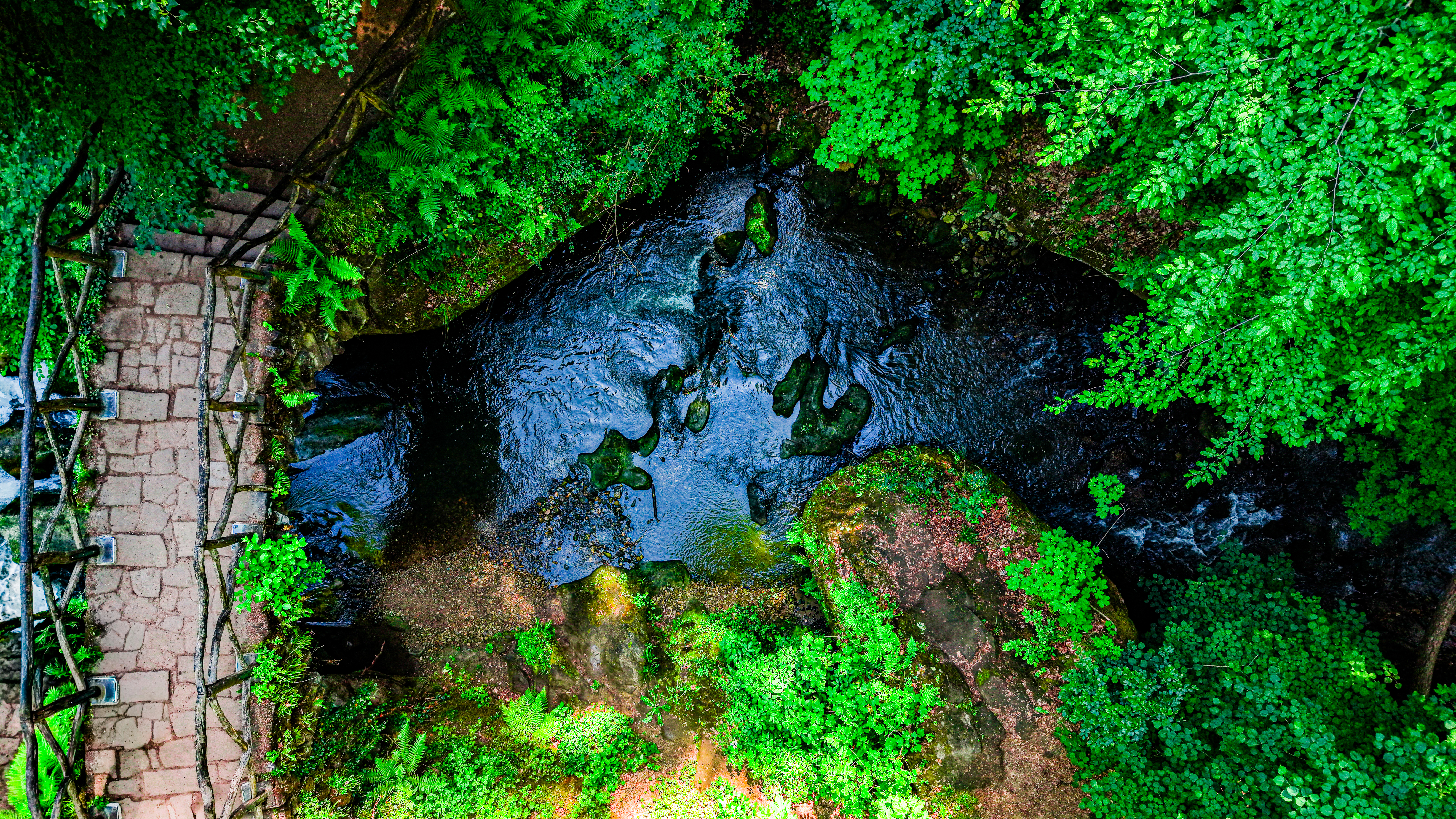 The old bridge and the Black Ernz from low altitude — stone arch, dark water, and the canopy pressing in on both sides. The gorge keeps the light off the water for most of the day; this shot required the gap when it briefly reached the bridge.