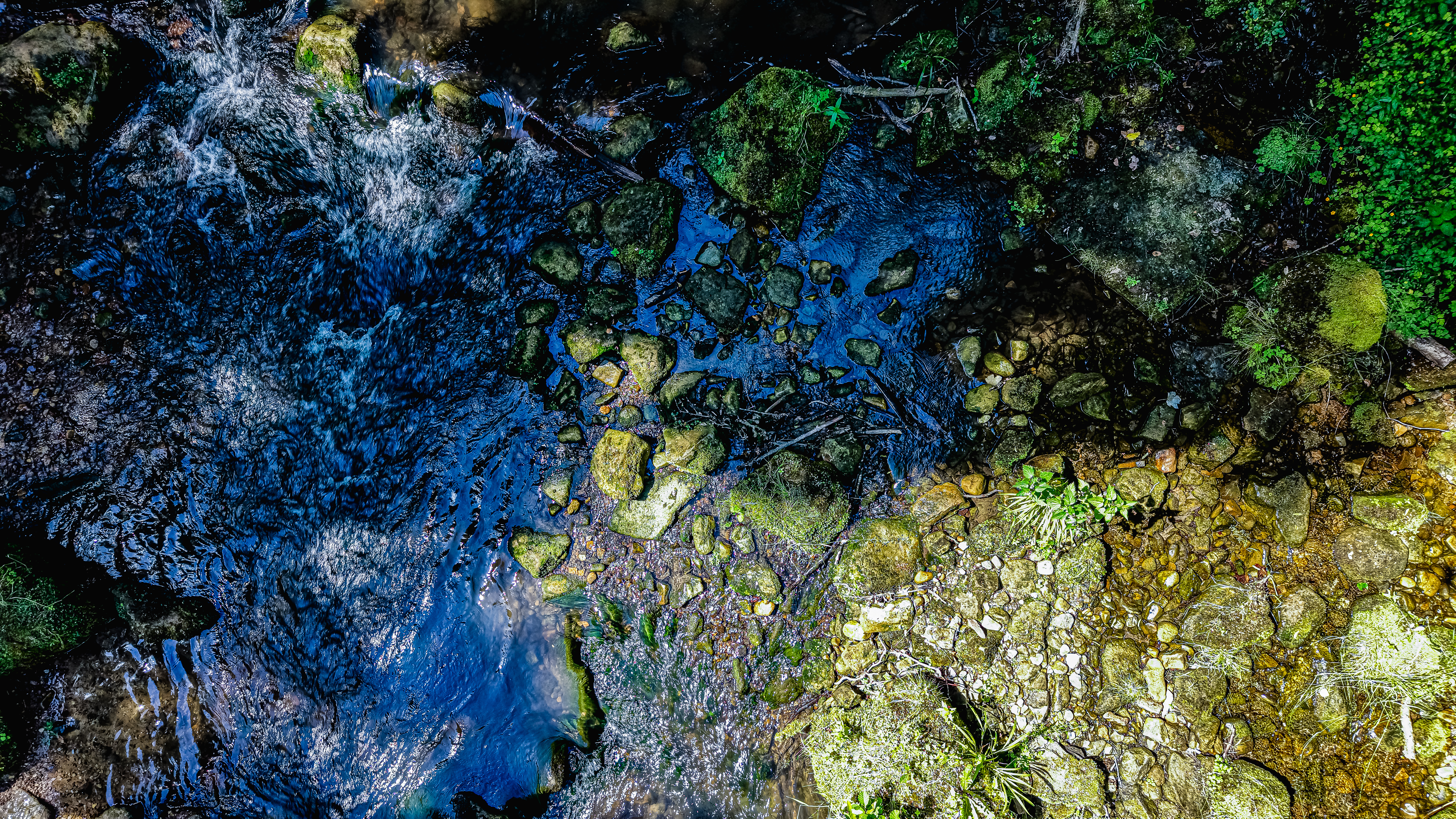 Streambed from directly above — the precise line where shallow amber water gives way to deep blue-black channel. The same river, two depths, two colors. At this altitude the Black Ernz reads as an abstract.