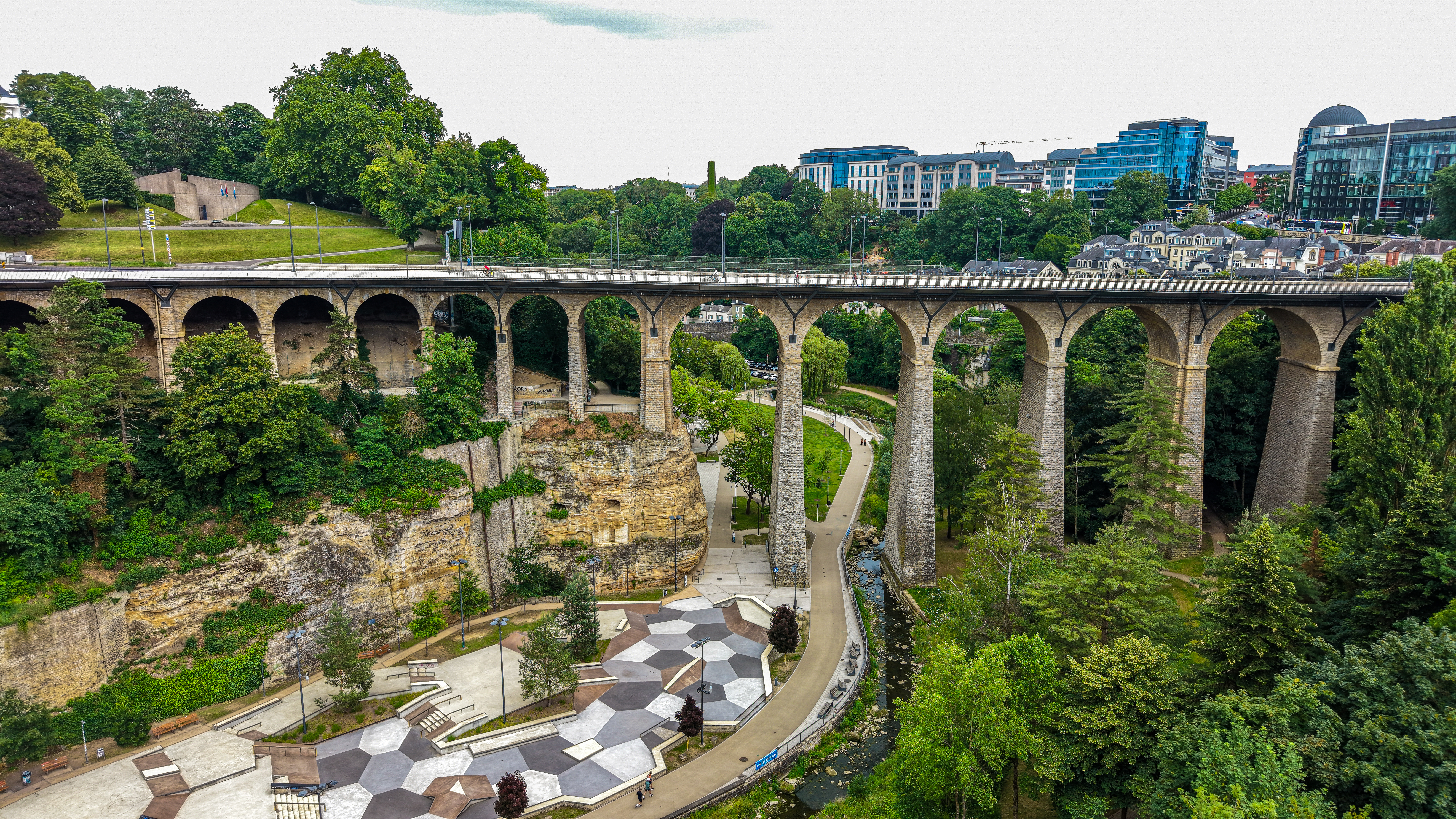 The Passerelle from the side — sandstone cliff face, twenty-four arches, gorge depth. The skate park in the lower left has occupied this shadow since 2021. The viaduct has been casting it since 1861.